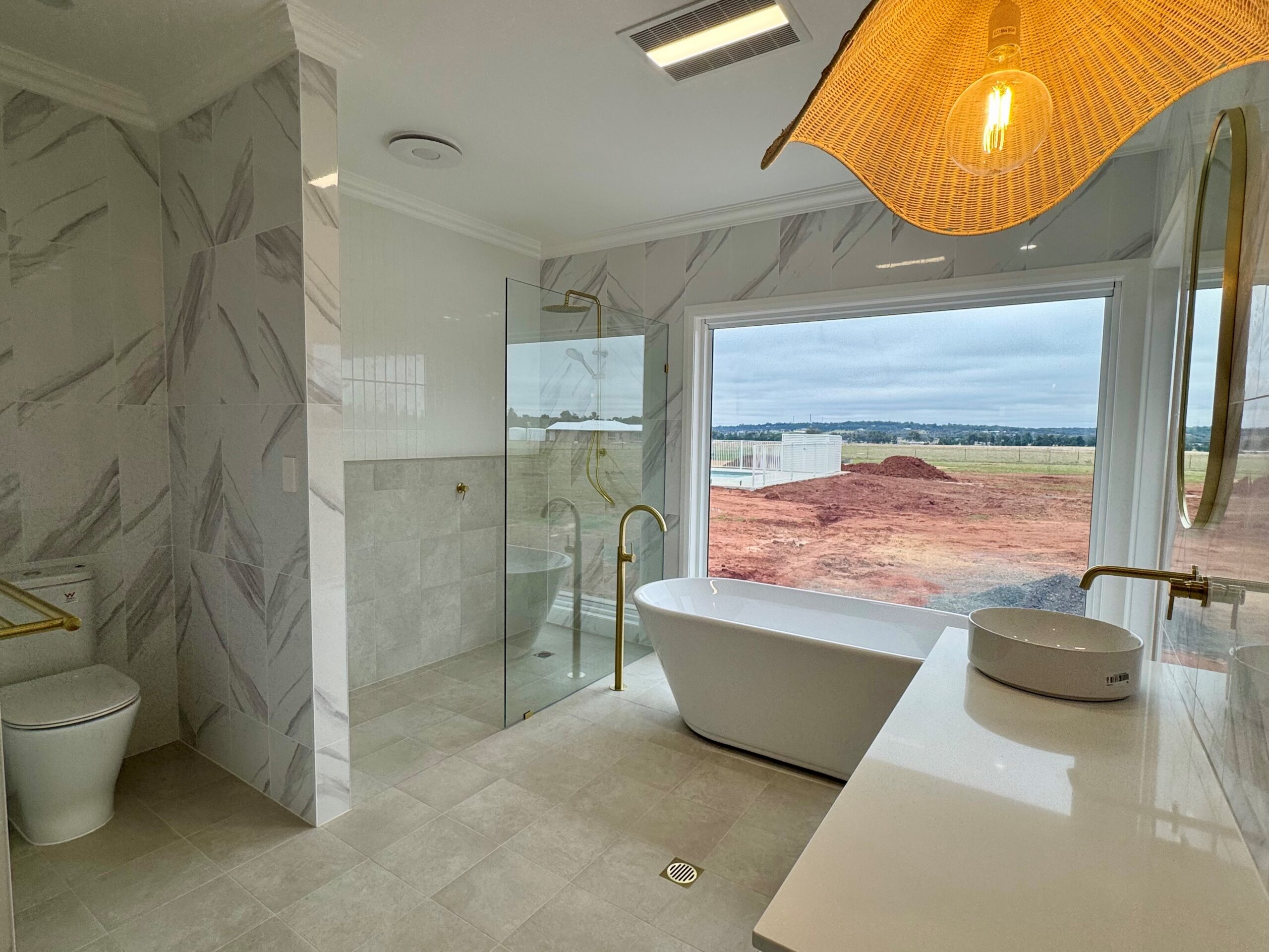 Ensuite with a freestanding bath and a window looking out over bare red soil on a new Dubbo estate